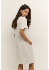 Jasno beżowa sukienka z lnu o luźnym kroju, krótkich rękawach, okrągłym dekolcie i bocznych kieszeniach. Subtelna tekstura z płynącym fasonem.