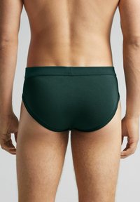 Bañador en color verde oscuro con una textura suave y elástica, de corte bajo, que cuenta con una cinturilla sencilla y costuras mínimas.