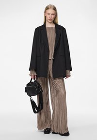 Blazer noir oversize, haut beige plissé et pantalon à pattes d'éléphant, associés à un petit sac noir, en tissu texturé et avec des accents minimalistes.