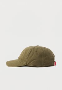 Gorra de béisbol verde oliva hecha de tela texturizada; cuenta con una visera curva y una pequeña etiqueta roja en el lateral. Sin patrones ni adornos visibles.