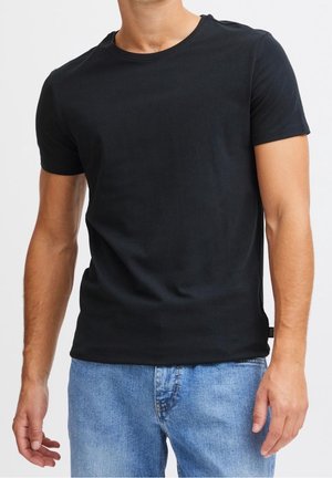 Schwarzes T-Shirt mit kurzen Ärmeln aus weichem Stoff, ausgestattet mit einem klassischen Rundhalsausschnitt und einem schlanken Schnitt. Kombiniert mit hellblauen Jeans.