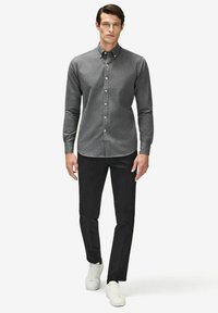 Mörkgrå skjorta med knäppning och standardkrage, kombinerat med svarta byxor och vita sneakers. Slät textur, figurnära design, klassisk stil.