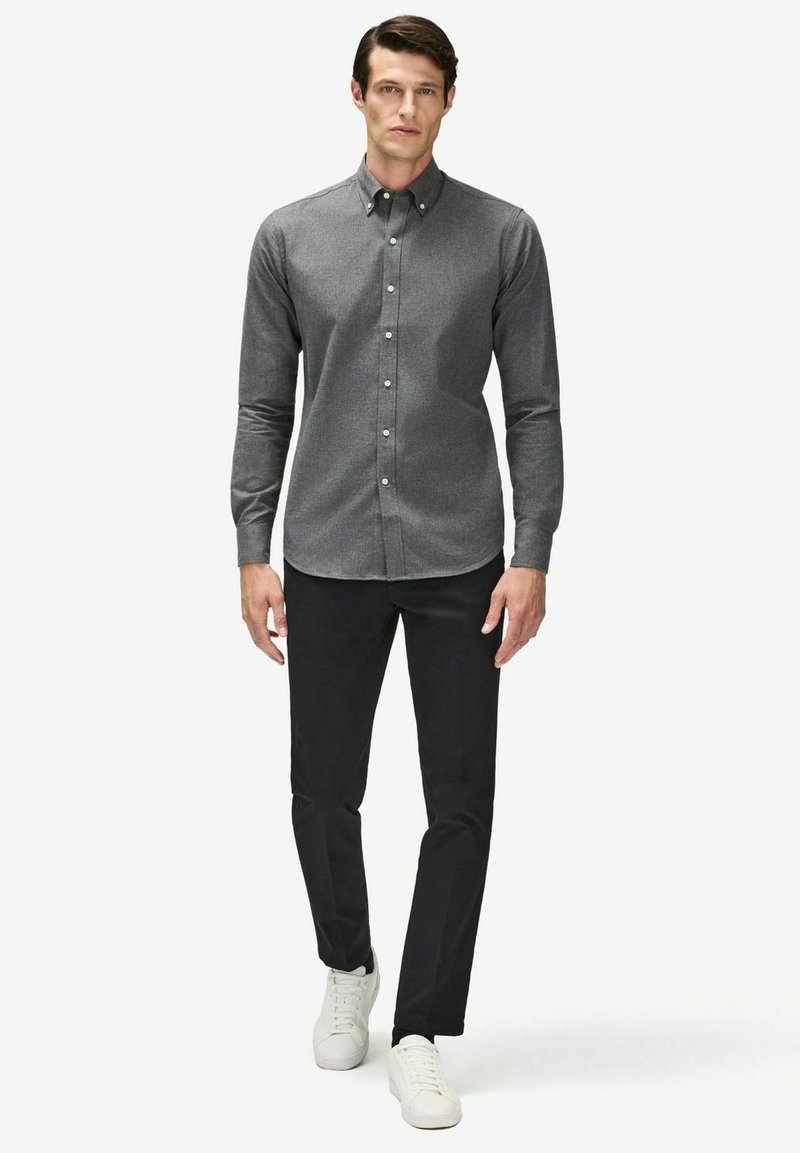 Mörkgrå skjorta med knäppning och standardkrage, kombinerat med svarta byxor och vita sneakers. Slät textur, figurnära design, klassisk stil.