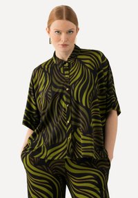 Short-sleeve button-up shirt featuring a black fabric with bold green wave patterns. Lightweight and relaxed fit, paired with matching patterned pants.