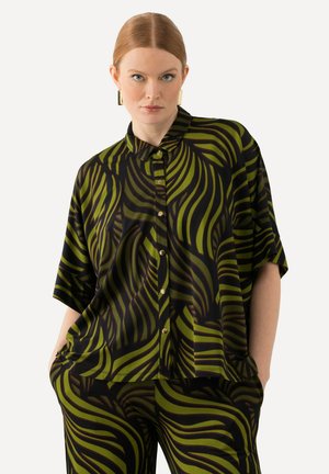Kurzarmpoloshirt aus schwarzem Stoff mit kräftigen grünen Wellenmustern. Leicht und lässiger Schnitt, kombiniert mit dazu passenden gemusterten Hosen.