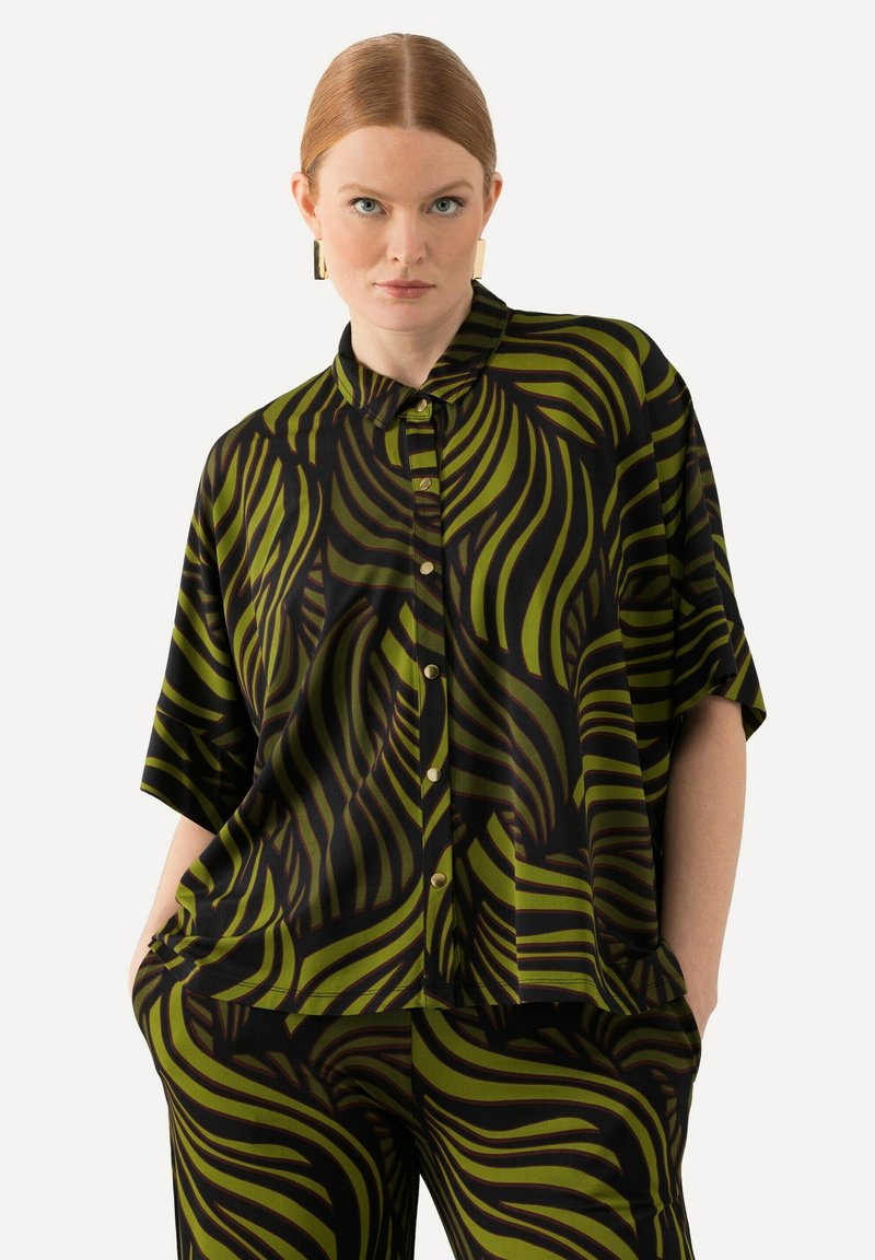 Short-sleeve button-up shirt featuring a black fabric with bold green wave patterns. Lightweight and relaxed fit, paired with matching patterned pants.