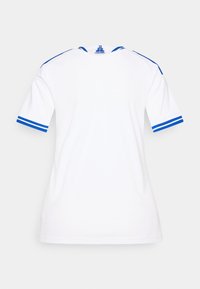 Λευκή μπλούζα με κοντά μανίκια και μπλε ρίγες στα μανίκια και το γιακά. Κατασκευασμένη από απαλό ύφασμα· διαθέτει λογότυπο στο πίσω μέρος του λαιμού.