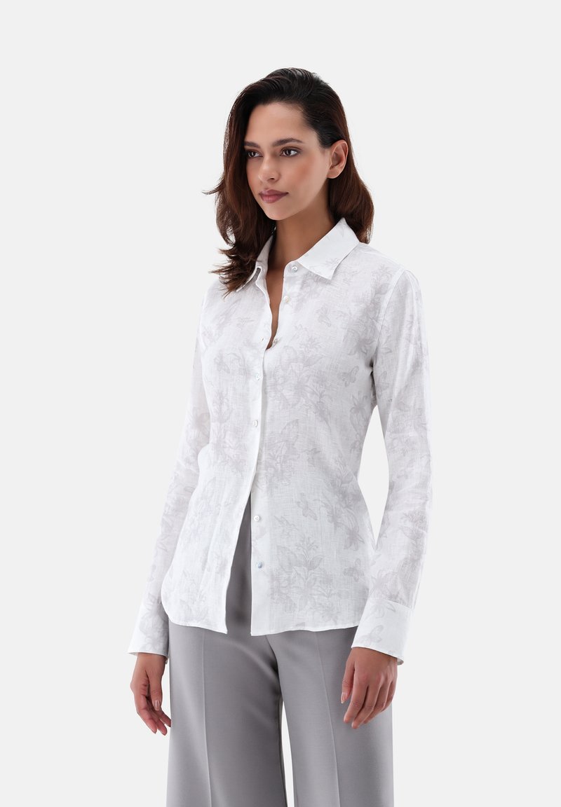 Camicia bianca a maniche lunghe con un sottile motivo floreale, dotata di colletto con bottoni, realizzata in tessuto leggero e con bottoni blu a contrasto.