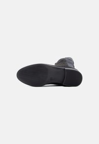 Black footwear with a textured rubber sole, featuring a smooth upper material and a modern design. The outsole has a distinct patterned tread.