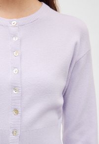 Μωβ-λιλά πλεκτή ζακέτα με στρογγυλή λαιμόκοψη, με ριμπ ύφανση και έξι κουμπιά στο εμπρός μέρος. Μαλακή υφή και εφαρμοστή σιλουέτα.