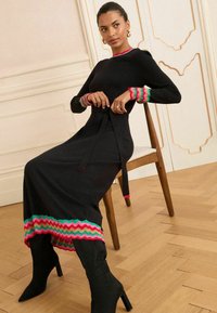 Abito nero a maniche lunghe con una silhouette aderente, caratterizzato da accenti zigzag multicolori sui polsini e sull'orlo, e un dettaglio in vita con fiocco.