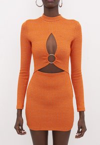 Robe mini à manches longues orange avec une ouverture en forme de goutte d'eau. Elle présente un accent anneau à la taille et un motif texturé sur tout le tissu.