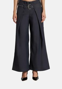 Pantalones de pierna ancha en tela gris oscuro con un diseño estructurado, un cinturón grande y pliegues laterales para un detalle adicional. Zapatos negros completan el look.