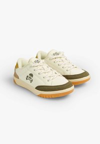 Weiße Sneaker mit olivgrünen Wildlederakzenten, strukturierten Schnürsenkeln und einer gelben Fersenschlaufe. Mit einem Totenkopf-und-Knochen-Logo an der Seite.