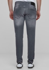 Szürke farmernadrág, slim fit szabásban, öt zsebbel és finom, kopott hatással. A hátulján fekete címke található, valamint látható varrási részletek.