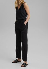 Svart ärmlös topp med v-ringning som matchas med löst sittande svarta byxor med elastisk midja och fickor, kompletterat med svarta platta sandaler.