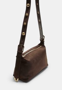 Braune Wildleder-Crossbody-Tasche mit einem Reißverschluss, ausgestattet mit einem breiten Tragegurt mit vergoldeten Nieten und einer Metallschnalle. Glatte Textur und rechteckige Form.