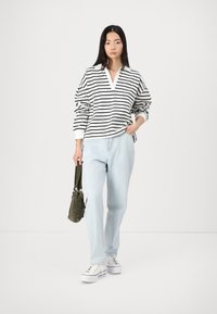 Hvit og svartstripet oversized hettegenser, v-halsdesign, kombinert med lyseblå baggyjeans og hvite sneakers. Grønn skulderbag som detalj.