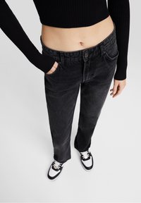 Jeans de mezclilla negra con un corte relajado, diseño de cinco bolsillos, un ligero desgaste y cierre de botón, combinados con zapatillas en blanco y negro.