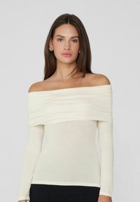 Cremefarbene, schulterfreie Bluse mit langen Ärmeln, die über dem Brustbereich geraffte Details und eine taillierte Silhouette aufweist. Glatte Textur.