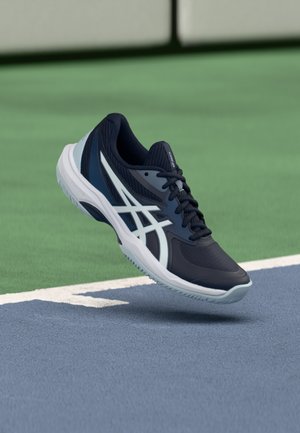 Tumesinine sportlik jalanõu, mis on valmistatud võrgust ja kummist, halli aktsendiga, paeltega ning tekstureeritud tallaga, paigutatud tenniseväljaku kohale.