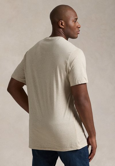 Ljusbeige t-shirt med korta ärmar i mjukt tyg, med rund halsringning och avslappnad passform, kombinerad med mörka jeans i denim.