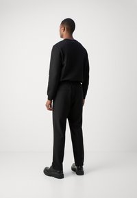 Sweat-shirt noir à col rond, coupe ajustée et poignets côtelés, associé à un pantalon noir avec une taille élastique et des poches.