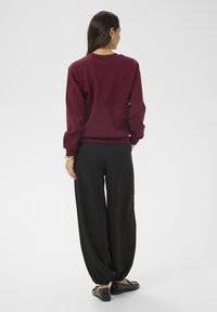 Burgundská mikina s kulatým výstřihem spárovaná s černými kalhotami širokého střihu a černými balerínami, s hladkou texturou a volným střihem.