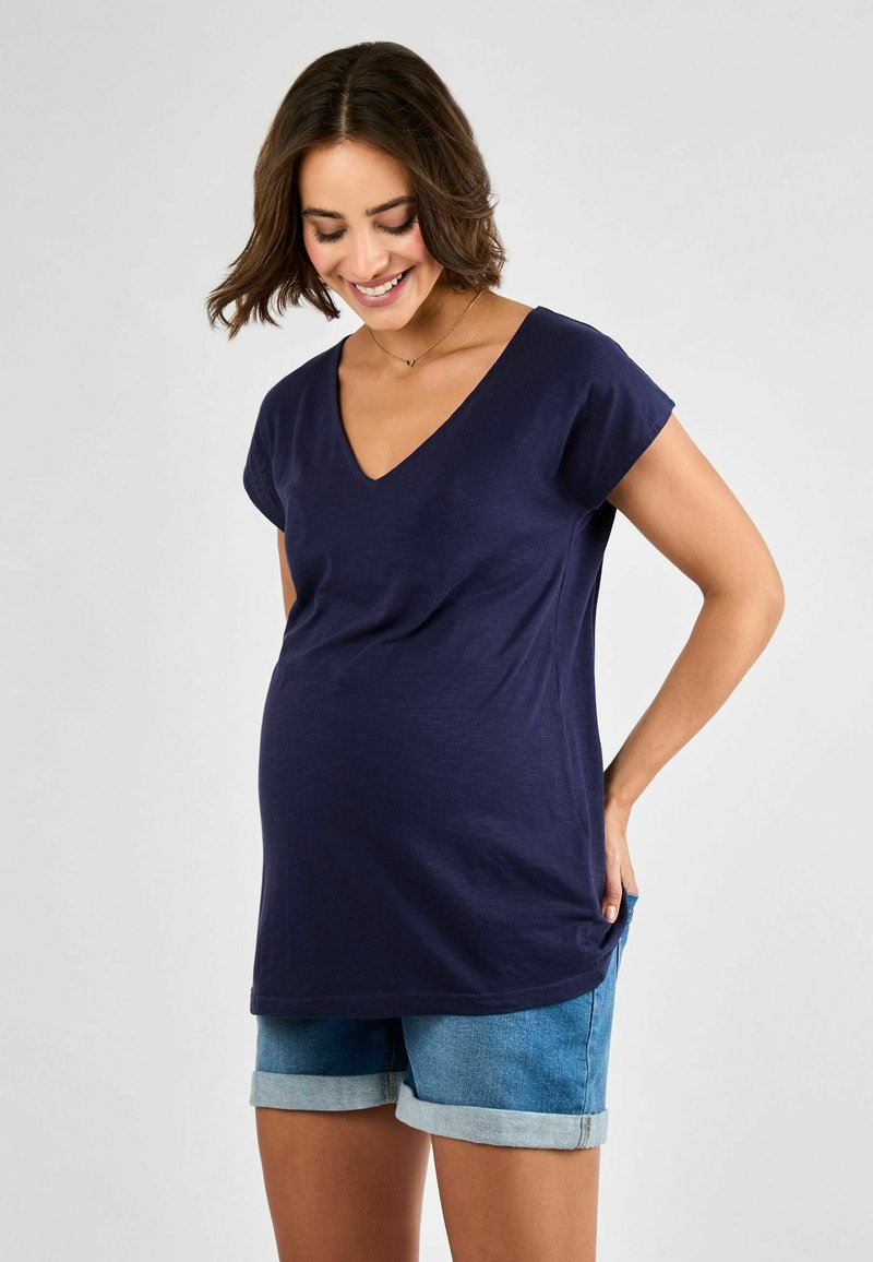 Maglietta premaman blu navy con scollatura a V, maniche corte e vestibilità comoda, abbinata a pantaloni corti in denim chiaro con risvolti.