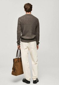 Brown knitted sweater with a cable pattern, paired with white trousers and a brown tote bag. The bag has dark handles and a sleek design.