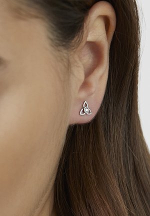 Small silver triquetra stud earring with a white center worn on the lower earlobe next to brown straight hair.