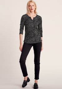 Zwarte longsleeve top met een wit abstract patroon, voorzien van een henley halslijn, 3/4 mouwen en slim-fit zwarte broeken, gecombineerd met zwarte instappers.