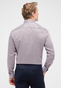 Langarmshirt van een witte, rode en marineblauwe patroonstof. Kenmerkt zich door een klassieke kraag en knoopsluitingen bij de manchetten. Getailleerde pasvorm.
