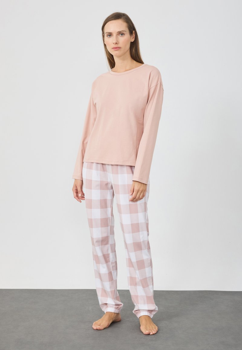 Haut rose clair à manches longues associé à un pantalon de pyjama à carreaux roses et blancs. Le pantalon comporte des poignets élastiques et une coupe décontractée. Texture de tissu douce.