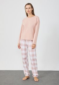Lyserød langærmet top parret med lyserøde og hvide ternede pyjamasbukser. Bukserne har elastiske manchetter og en afslappet pasform. Blød stofstruktur.