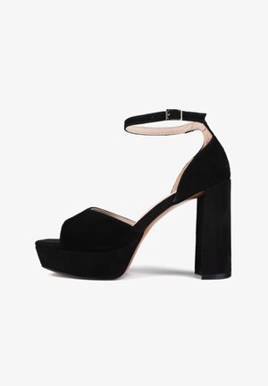 Schwarze Wildleder-Plateausandalen mit einem Knöchelriemen, die eine offene Zehenpartie und einen klobigen rechteckigen hohen Absatz aufweisen. Glatte Textur und schlichtes Design.