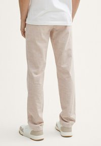 Pantalones beige claros hechos de tela suave, con corte recto, textura sutil y combinados con zapatillas deportivas blancas y beige.