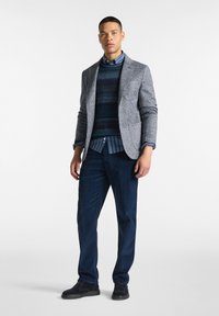 Blazer a scacchi grigi sopra un maglione navy testurizzato, abbinato a una camicia a righe blu e pantaloni in velluto a coste navy. Scarpe nere completano il look.