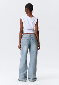 Witte mouwloze top gecombineerd met lichtblauwe, wijde jeans met achterzakken en contrasterende stiksels. Eenvoudige en relaxte pasvorm.