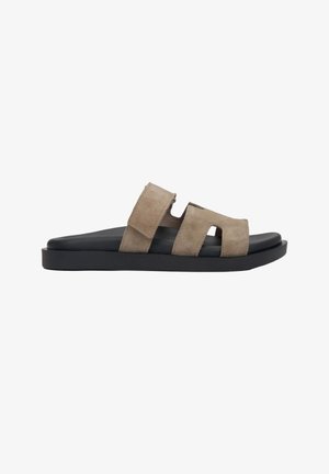 Slide sandal with black sole and two wide beige suede straps, one with a cutout and velcro closure, side view on white background.