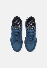 Blå sportskor med mocka och mesh-material, med rundad tå, snörning fram och en logotyp på tungan. Svart inredning.