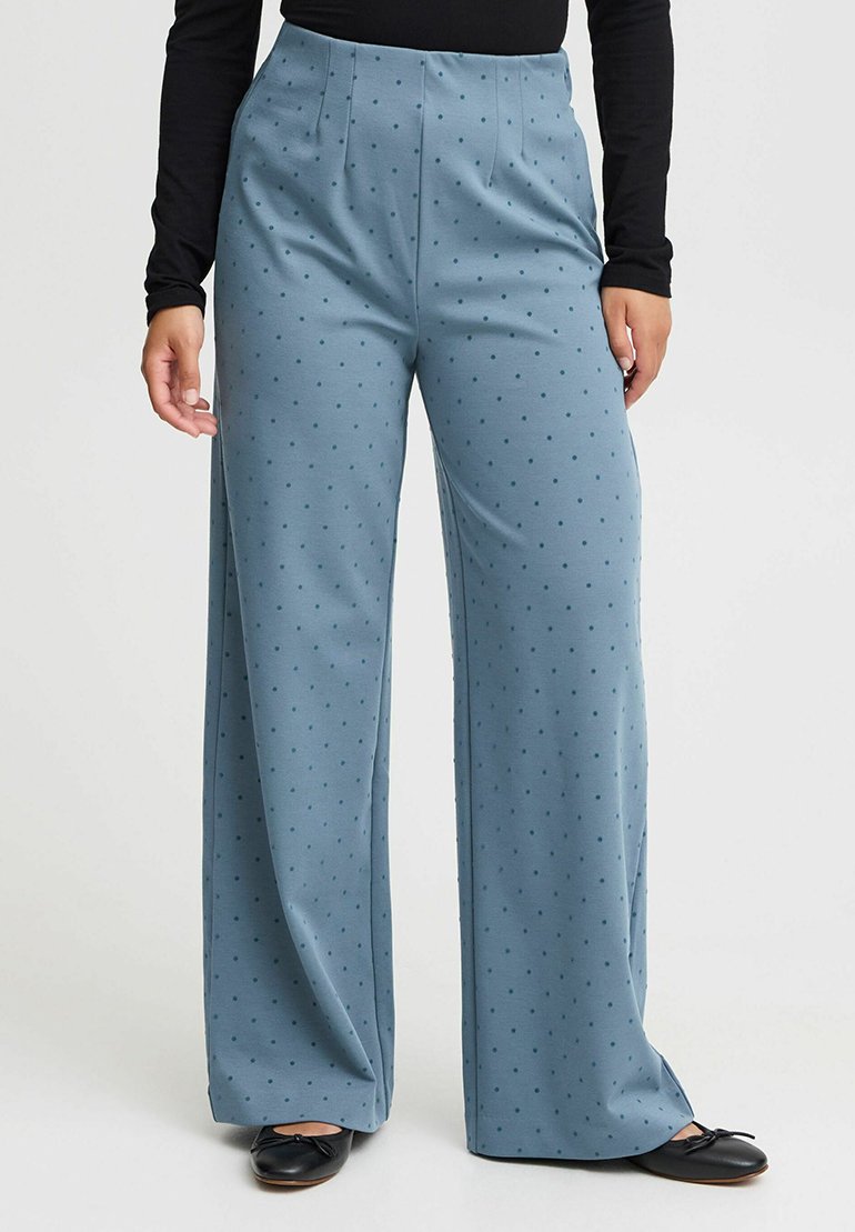 Wijdvallende broek in lichtblauwe stof met donkerdere stippen, met een hoge taille en plooidetails, gecombineerd met zwarte ballerina's.