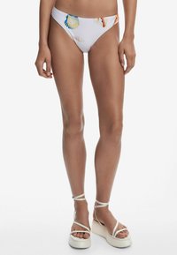 Biele spodné plavky v bikinách s farebnými vzormi mušlí. Spárované s bielymi platformovými sandálmi s členkovými remienkami a textúrovanou podrážkou.