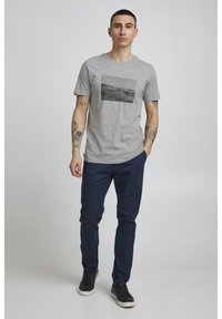 Camiseta gris con un gráfico rectangular en blanco y negro, combinada con chinos azul marino y zapatillas negras. Diseño simple y casual.