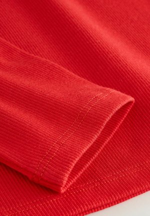 Roter, gerippter Stoff mit leichtem Textil, der einen umgeschlagenen Ärmelrand und dezente kontrastierende Nähte aufweist.