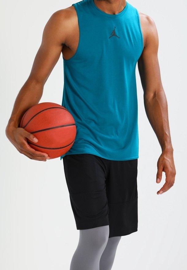 Uomo che indossa una maglietta senza maniche color turchese e pantaloni corti neri, mentre tiene un pallone da basket su uno sfondo chiaro e semplice.