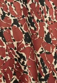 Tessuto di cotone con un audace motivo astratto in rosso, nero e beige, caratterizzato da forme irregolari e testurizzate, con una finitura morbida.