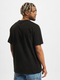 Black cotton t-shirt with a relaxed fit, round neckline, and short sleeves. Visible stitching and casual design. Worn with blue denim jeans.