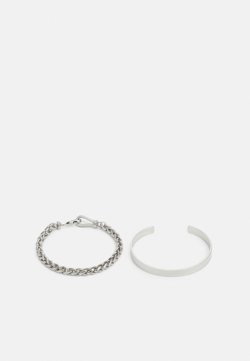 Pulsera de cadena de plata con un broche al lado de una pulsera de tipo cuff minimalista, ambas mostrando un acabado pulido y elegante con líneas limpias.