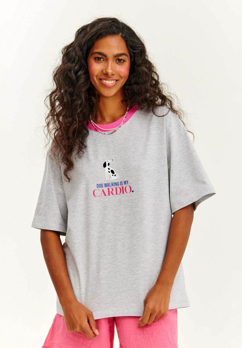 Šedé bavlněné tričko s krátkým rukávem, růžovým střihem na krku a potiskem textu "VENČENÍ PSA JE MÉ KARDIO" spolu s grafikou psa.